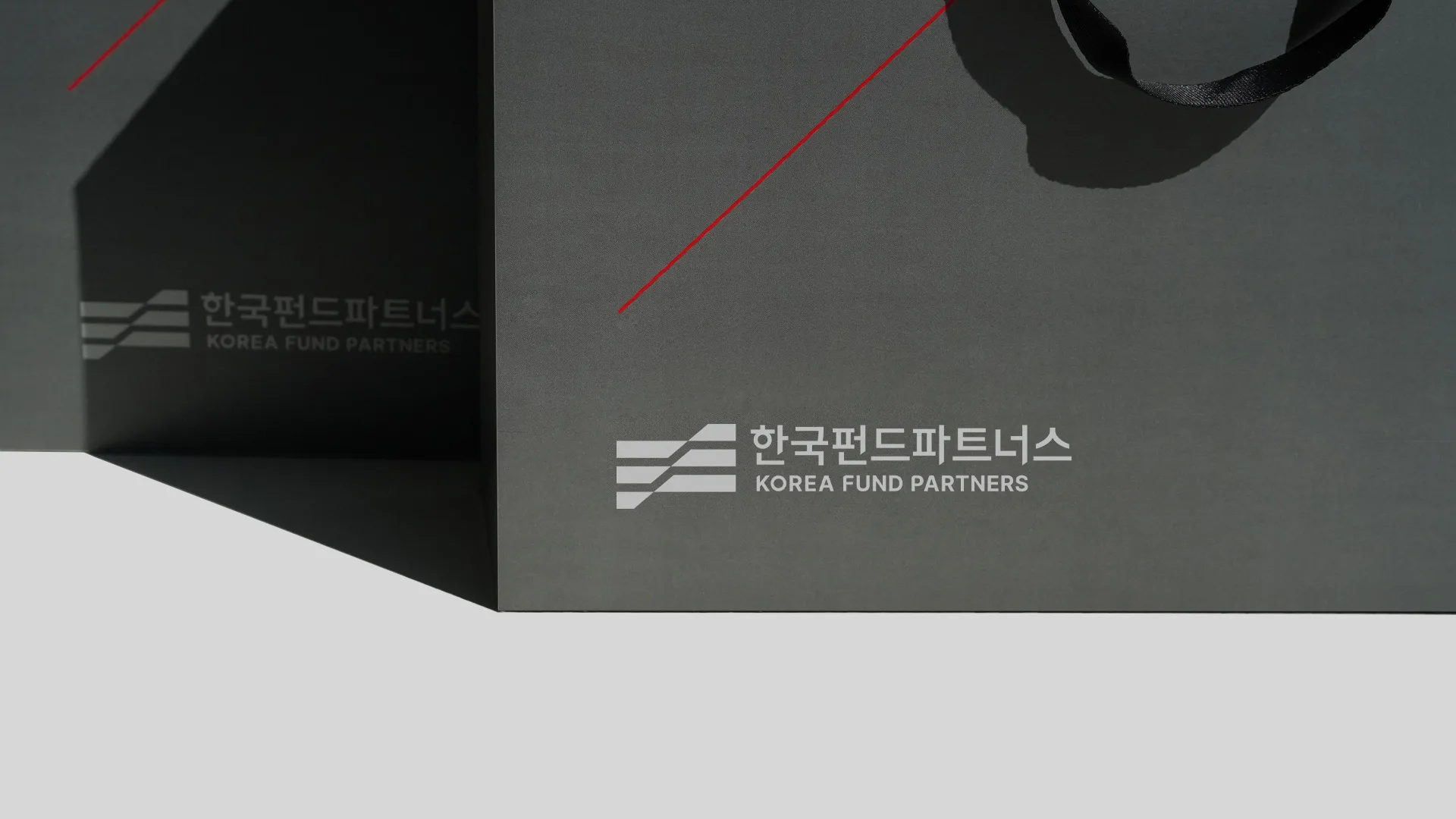 한국펀드파트너스의 로고가 선명하게 인쇄된 어두운 회색 쇼핑백으로, 브랜드의 전문성과 신뢰감을 전달합니다. 한국펀드파트너스 로고가 인쇄된 어두운 회색 쇼핑백 클로즈업