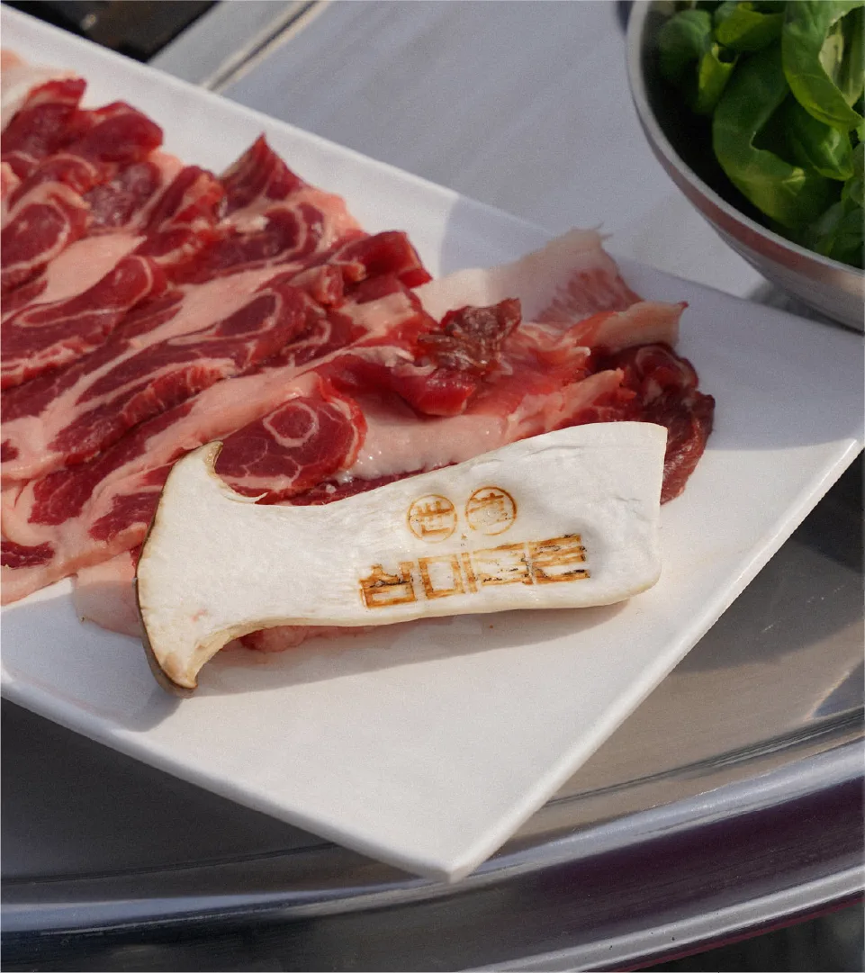 Fresh Sammi-Teukdon raw pork and king oyster mushroom branded with the logo. Offering an authentic gastronomic experience that respects nature's principles. Raw Sammi-Teukdon pork and king oyster mushroom with brand logo on white plate