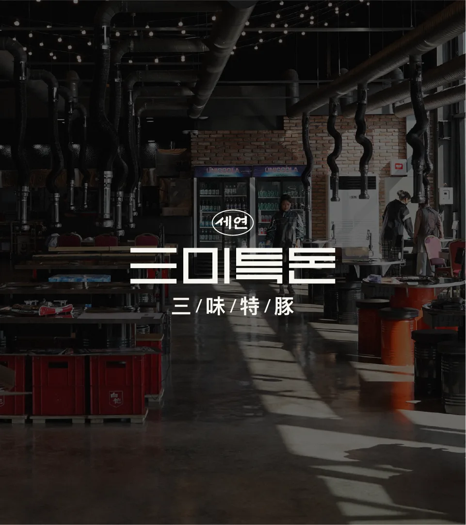 Interior view of Sammi Teukdon, Seyeon Chuksan's premium pork brand restaurant. The industrial interior combined with the logo showcases a modern yet fundamental brand identity. Dark restaurant interior with Sammi Teukdon logo overlay, industrial atmosphere.