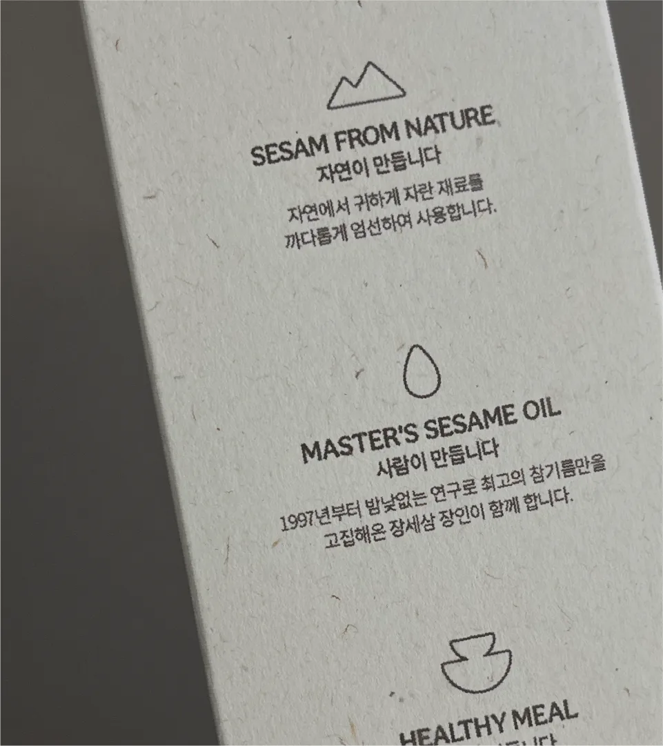 Brand story and product features printed on SESAM Oil House packaging. Text emphasizing natural ingredients and artisan know-how is neatly presented on textured paper. Close-up of SESAM Oil House product description text and icons on textured paper