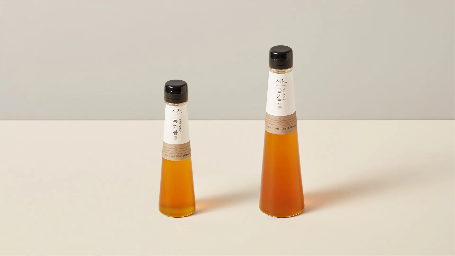 Sesam Perilla Oil products embodying the brand's neat and simple design philosophy. Offered in two sizes for versatility. Two bottles of Sesam Perilla Oil, one large and one small, on a light background