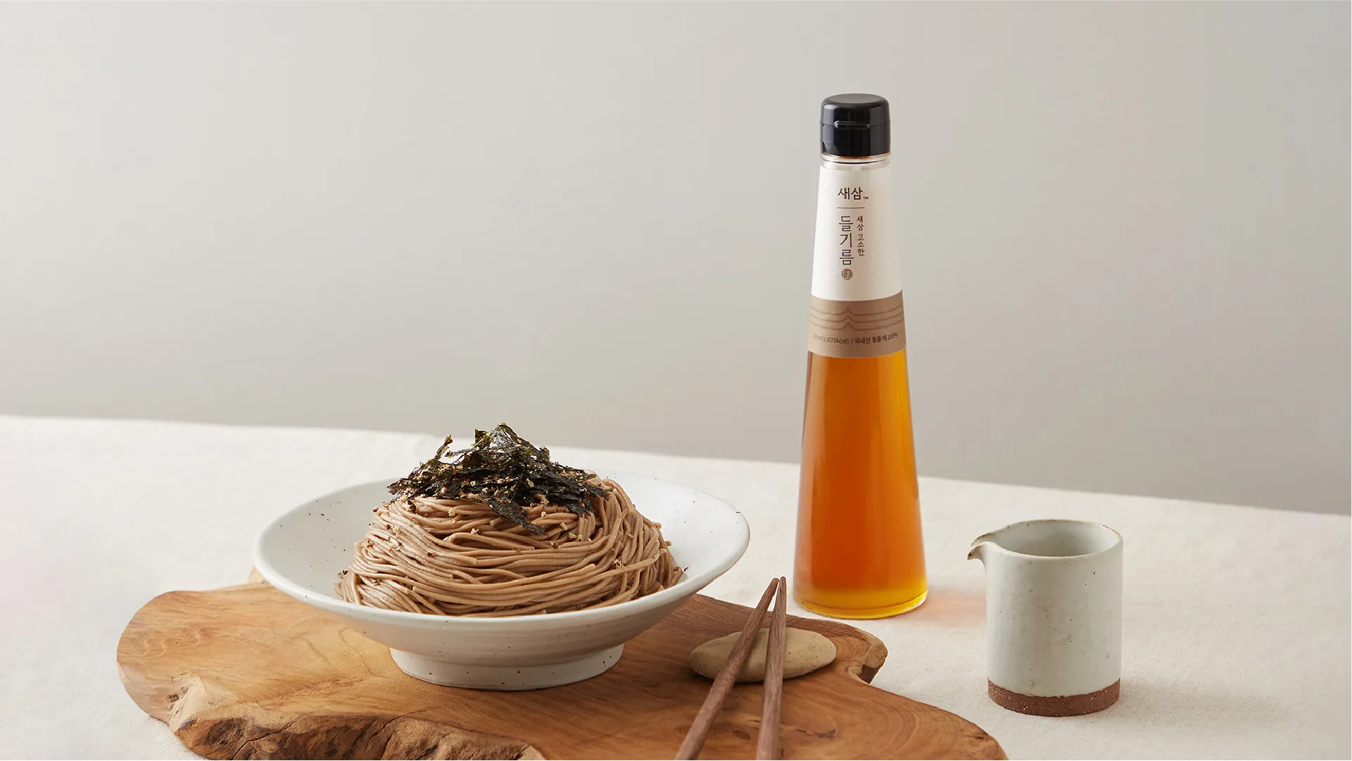 A healthy and refined meal with SESAM perilla oil. Proposing a premium lifestyle that reinterprets traditional flavors with a modern sensibility. SESAM perilla oil bottle, buckwheat noodles, chopsticks, and ceramic ware on a c