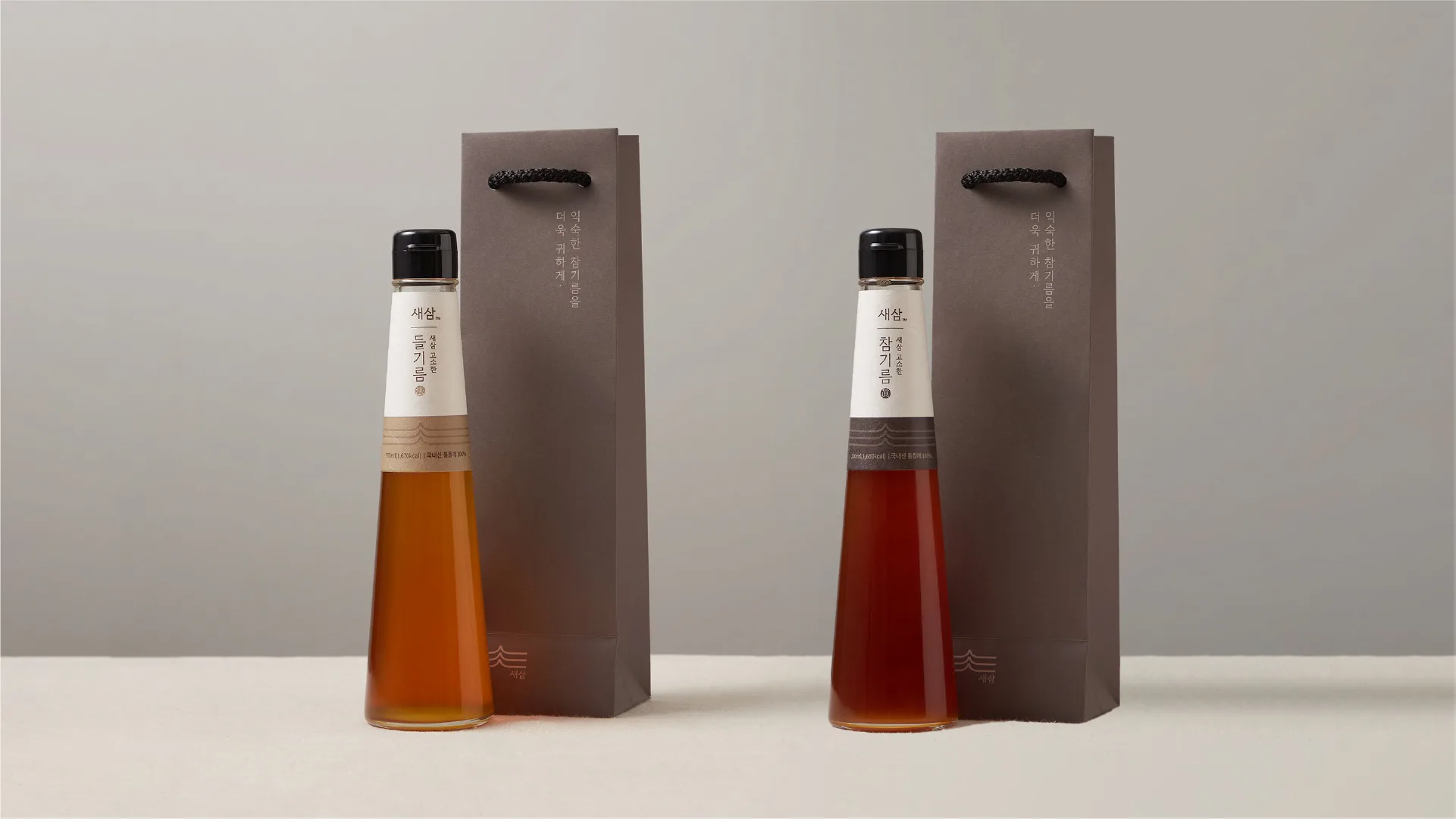 Sesam Oil House's premium sesame and perilla oil set. Showcasing a refined and sophisticated package design that elevates familiar oils. Two bottles of Sesam sesame and perilla oil with brown paper bags on a grey back